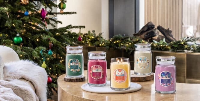 Julgran med färgglada kulor bredvid ett bord med doftljus i en festlig vintermiljö.