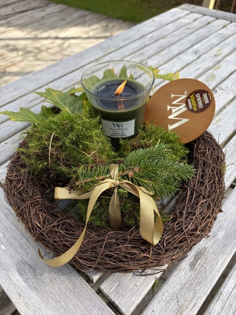 Dekorativ höstkrans med mossdekoration och brinnande ljus på träbord.